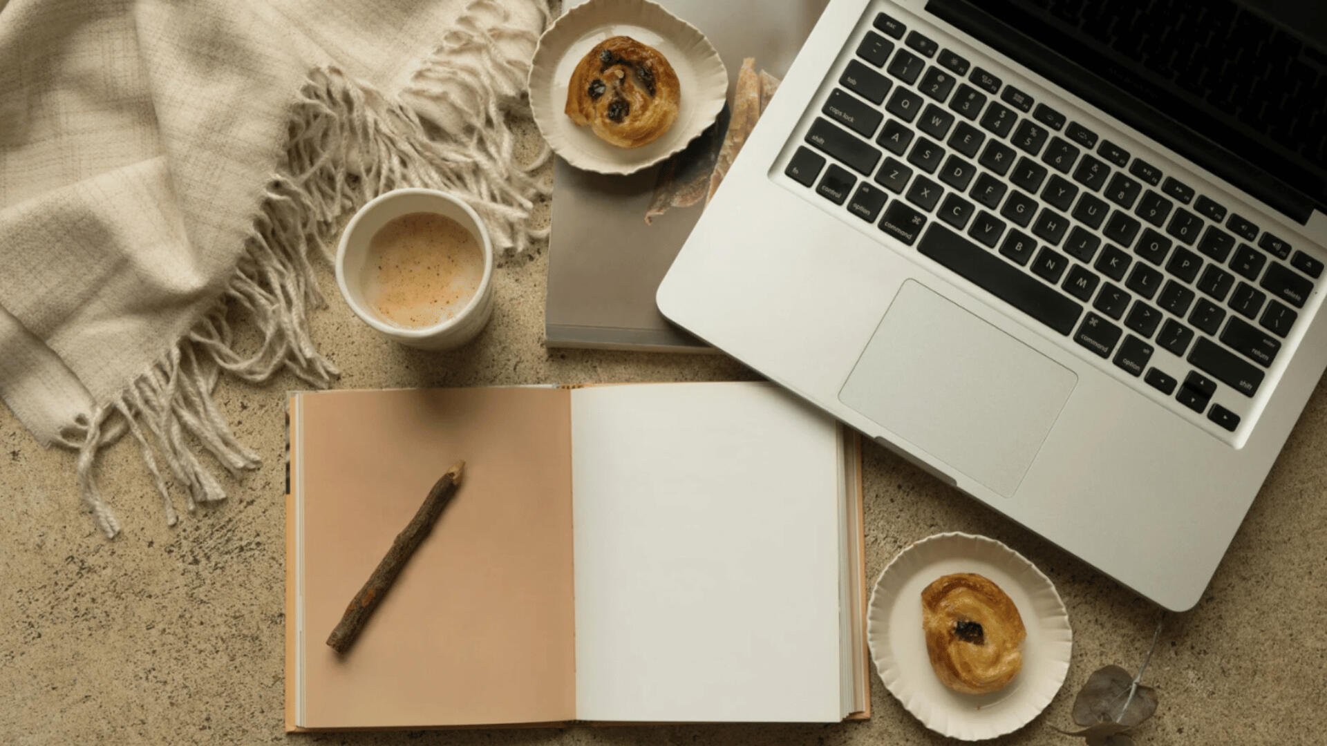 Your Creative Corner — Discover Tools to Spark Your Writing Process Flat lay of a writer’s workspace featuring an open notebook, pen, laptop, coffee cup, and pastries on a soft-toned desk with a woven throw—evoking warmth, focus, and creative flow.
