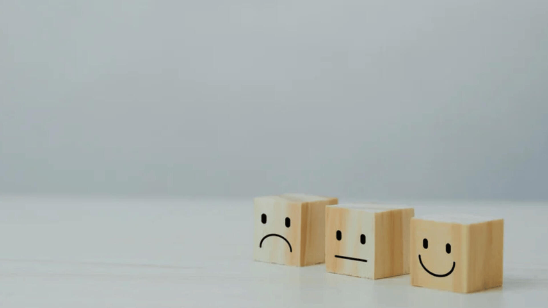 Support That Cares – From Questions to Resolution Three wooden blocks with faces showing a sad, neutral, and happy expression, placed in a row. Represents the range of customer experiences and Carlisha Writes & Co.’s commitment to support and resolution.